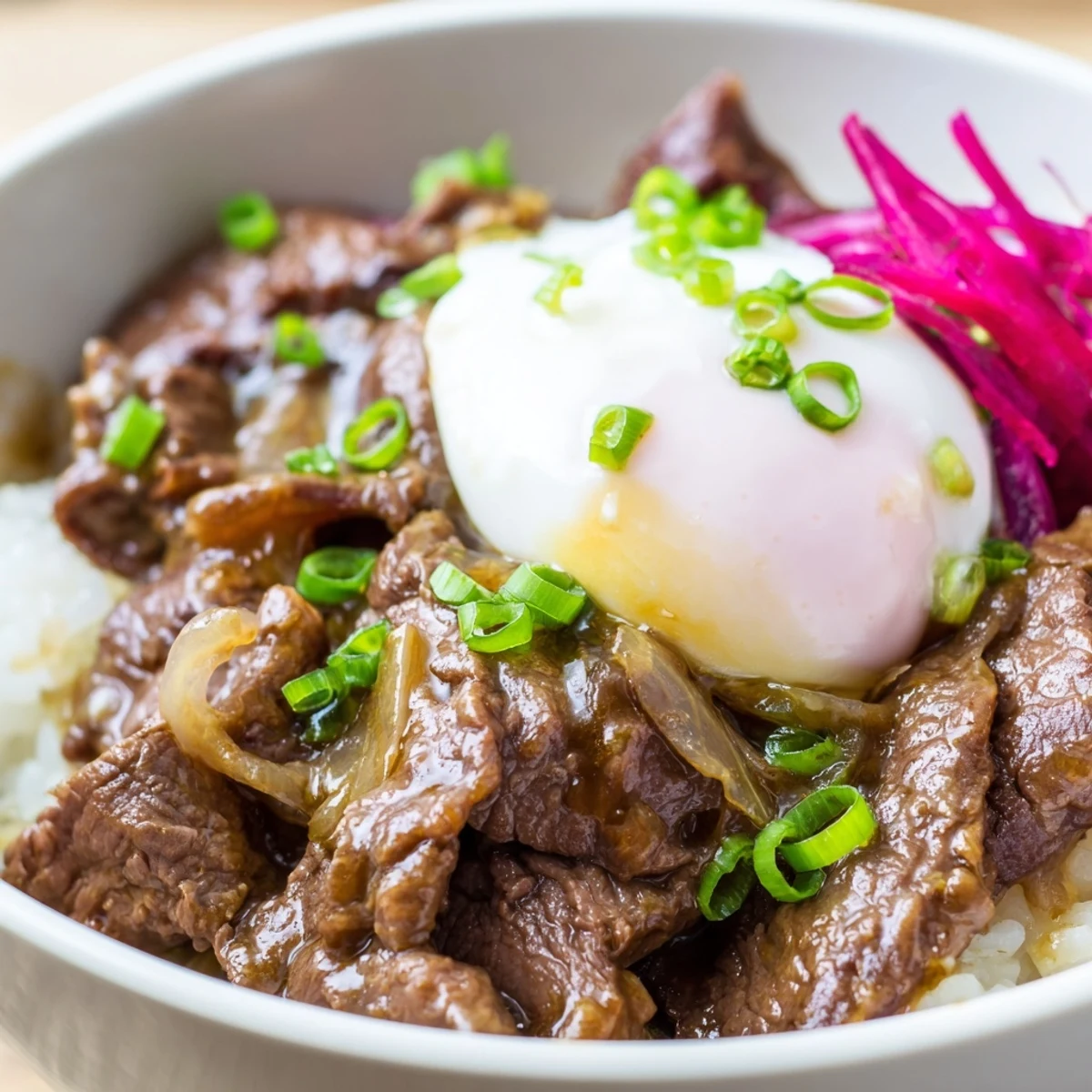 A close view of a comforting Beef Bowl with Rice, topped with tender beef, soft onions, and a fresh green onion garnish.