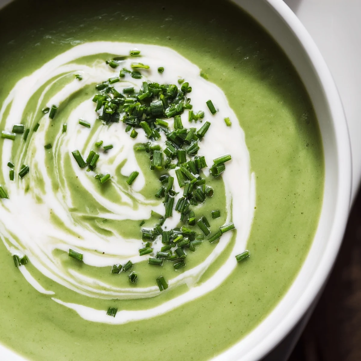 Steaming bowl of homemade Creamy Broccoli Soup with a wooden spoon and fresh broccoli florets nearby.