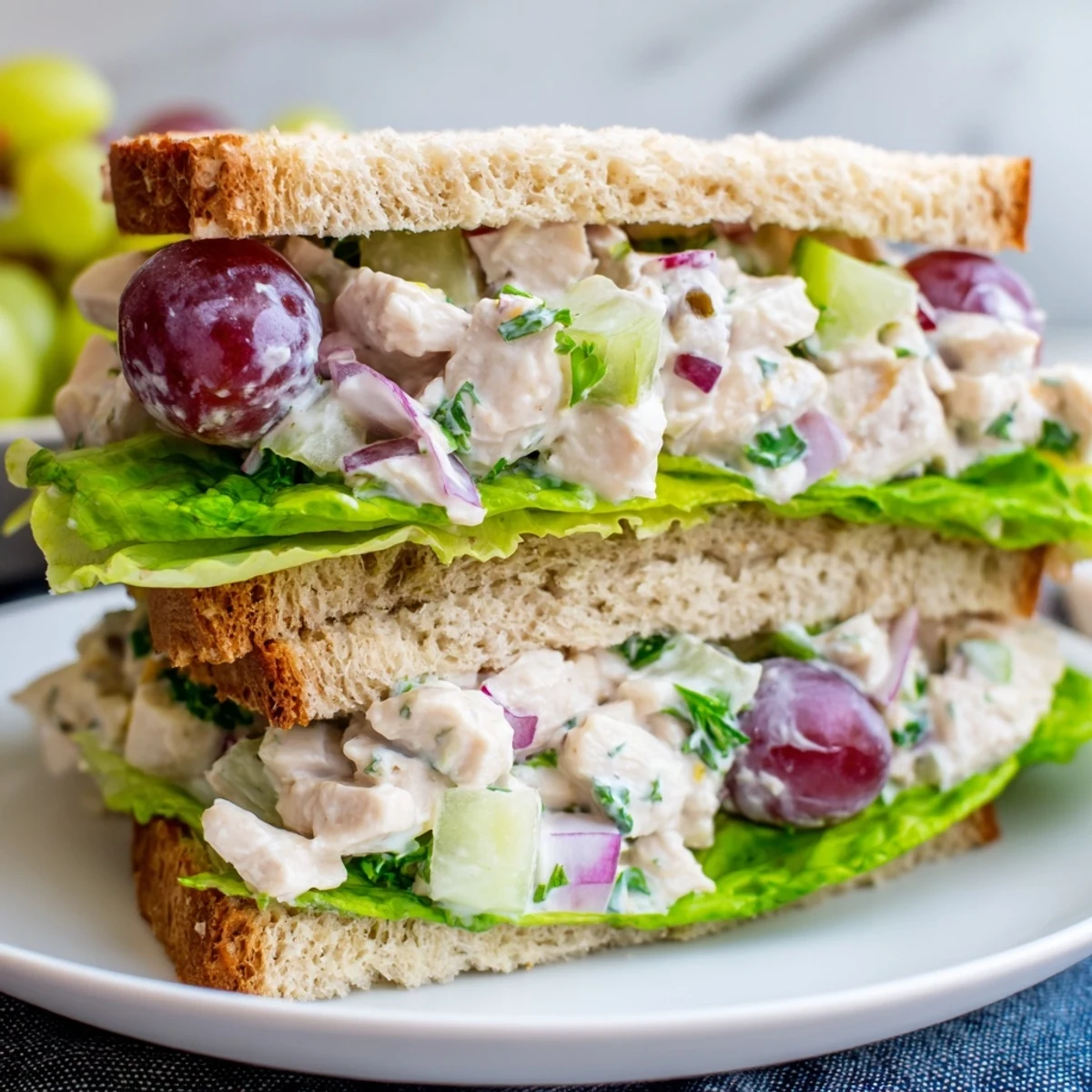 Close-up of a freshly made Chicken Salad Sandwich with Grapes on whole wheat bread, showing creamy chicken mixture and crisp lettuce.