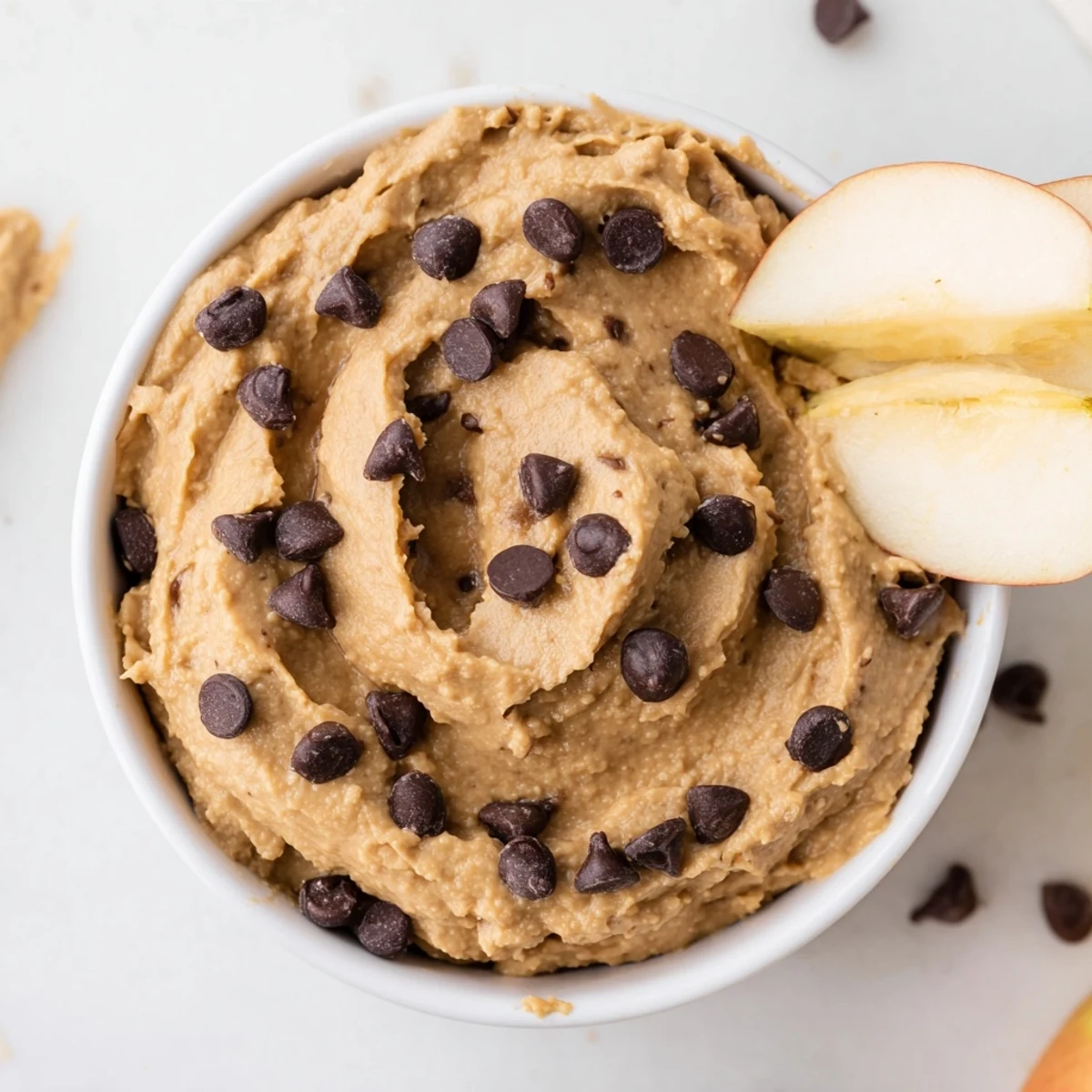 Creamy Chocolate Chip Cookie Dough Hummus in a bowl surrounded by crisp apple slices for sweet dipping.