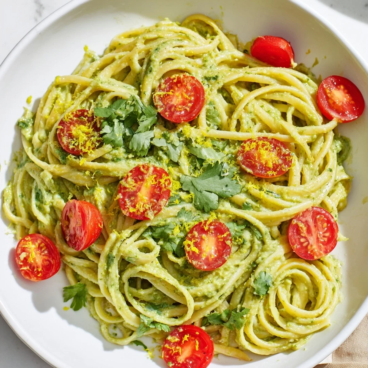 Bright green avocado sauce coats pasta noodles, with halved cherry tomatoes and a sprinkle of Parmesan cheese.