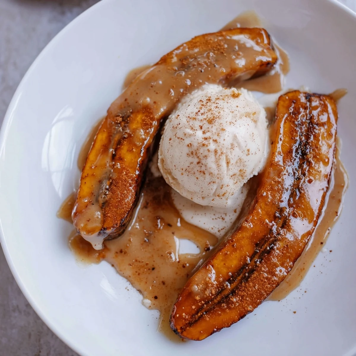 Golden caramelized Bananas Foster bubbling in a skillet, spooned over scoops of vanilla ice cream for a warm dessert.