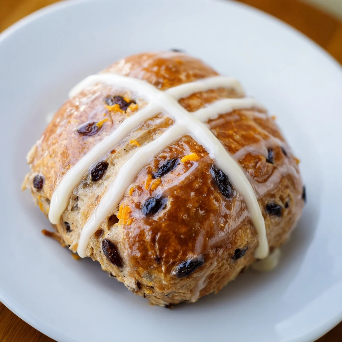 A close-up of freshly baked Hot Cross Buns featuring a glossy apricot glaze and a classic pastry cross.
