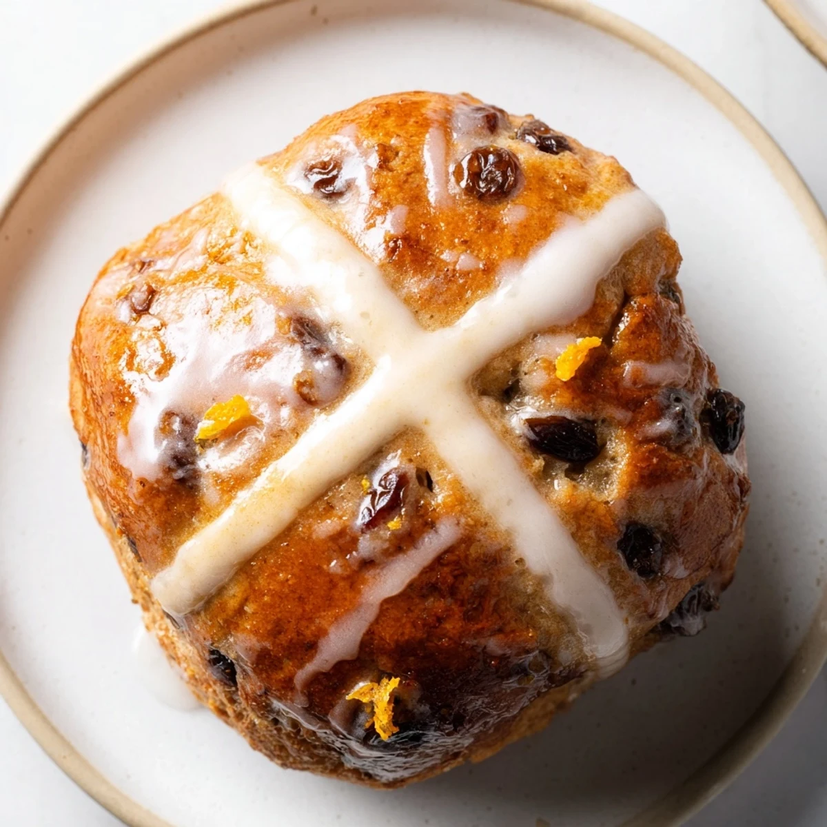 Warmly glazed Hot Cross Buns with raisins and orange zest sit on a rustic wooden board.