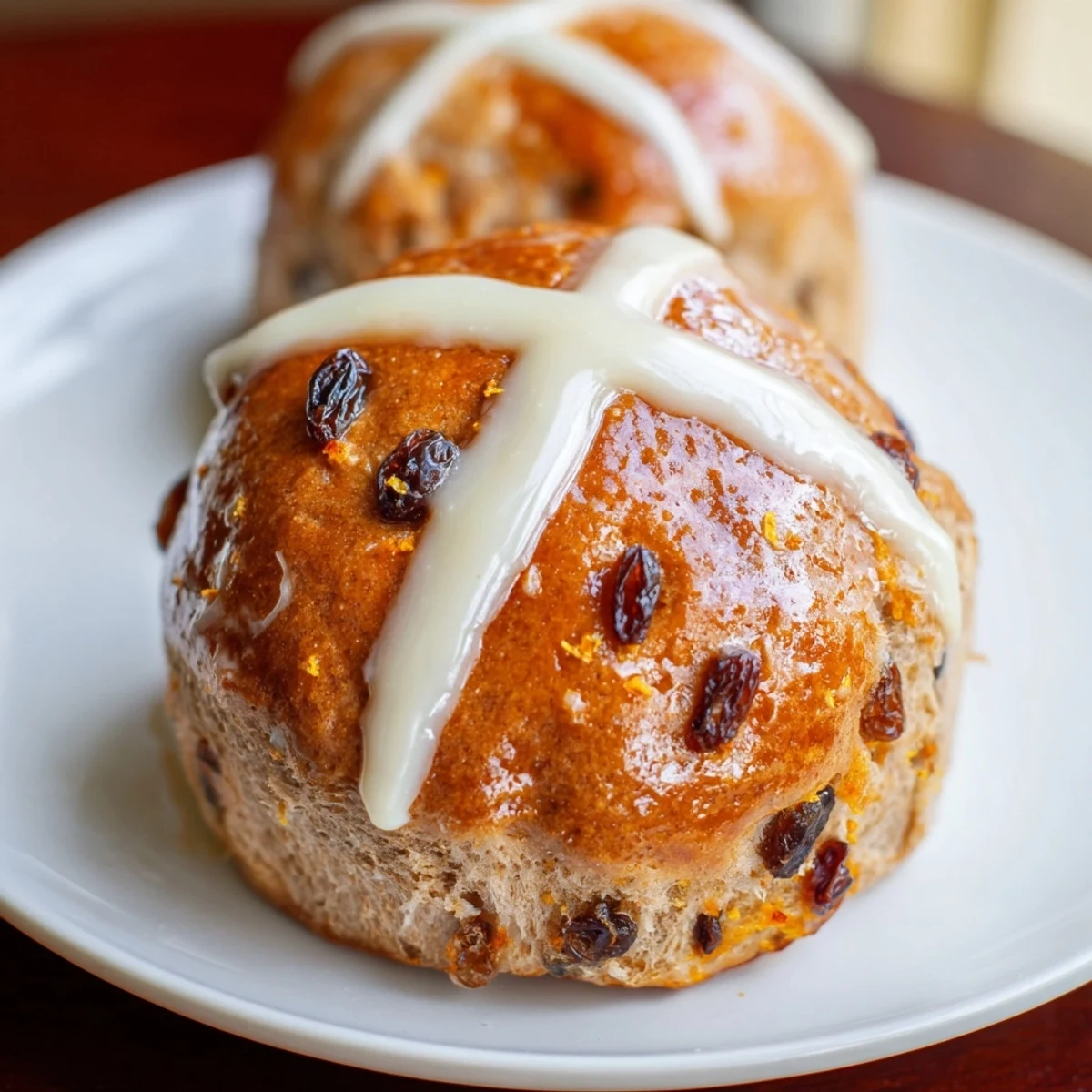 Golden brown Hot Cross Buns with raisins and orange glaze, arranged on a cooling rack in a home kitchen.