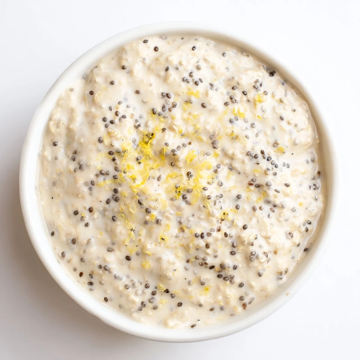 Creamy Vegan Lemon Poppy Seed Overnight Oats in a clear glass jar with fresh berries and sliced almonds on top.