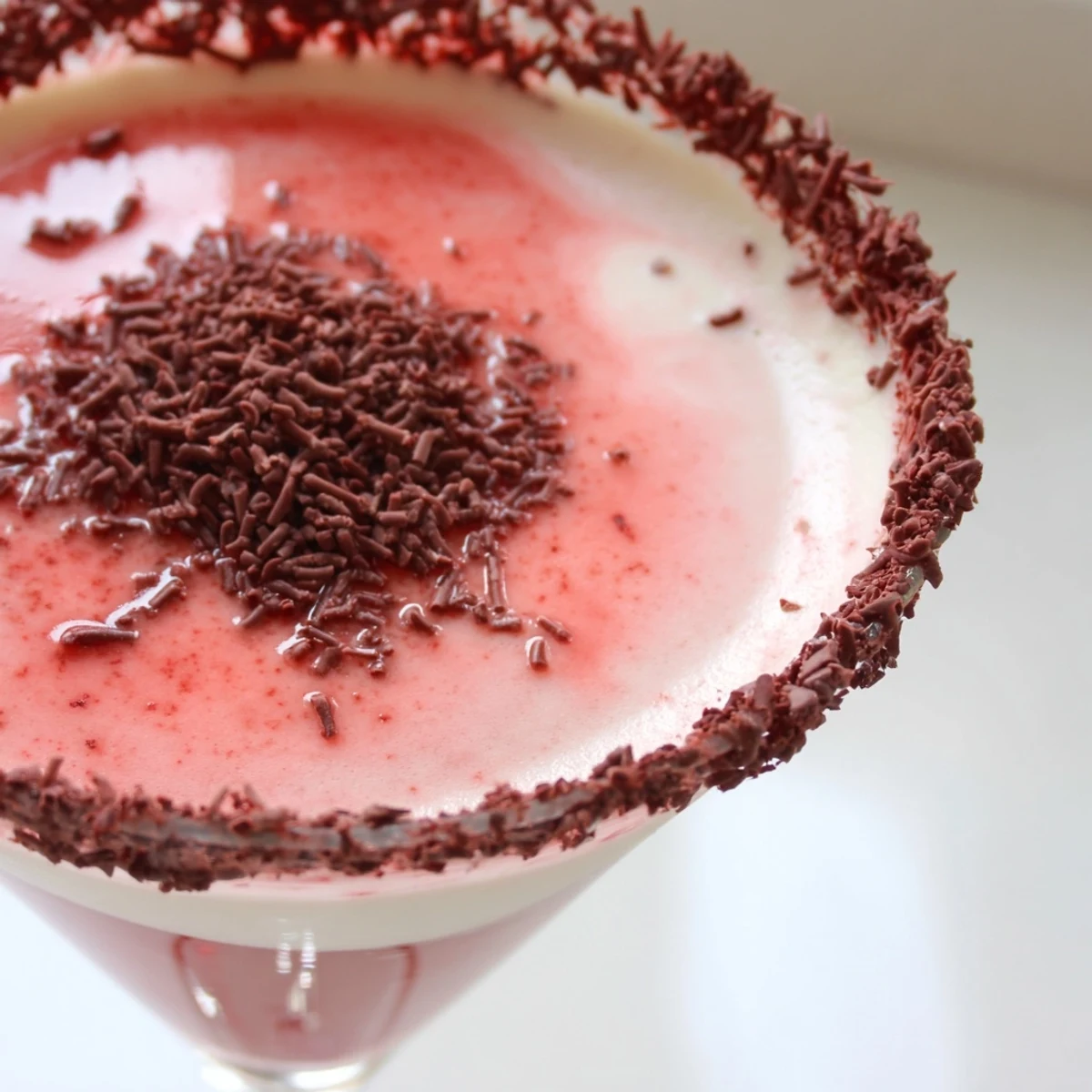In a dim restaurant ambiance, a Decadent Red Velvet Martini sits on a dark surface, showcasing its crimson hue and chocolate garnish.