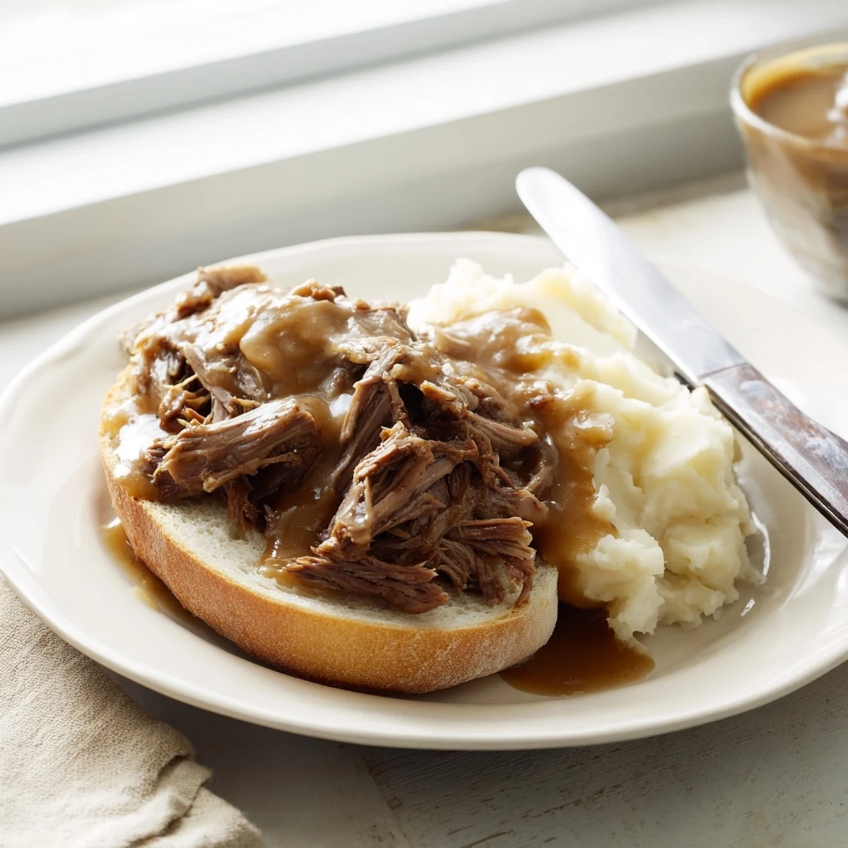 Slow Cooker Beef Manhattan presented on white bread with creamy mashed potatoes and rich brown gravy on a rustic table.