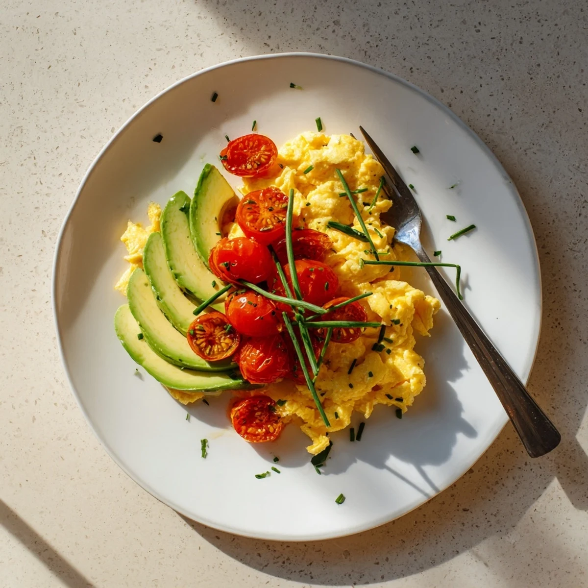 Fluffy scrambled eggs topped with creamy avocado and juicy seared tomatoes for a vibrant breakfast plate.