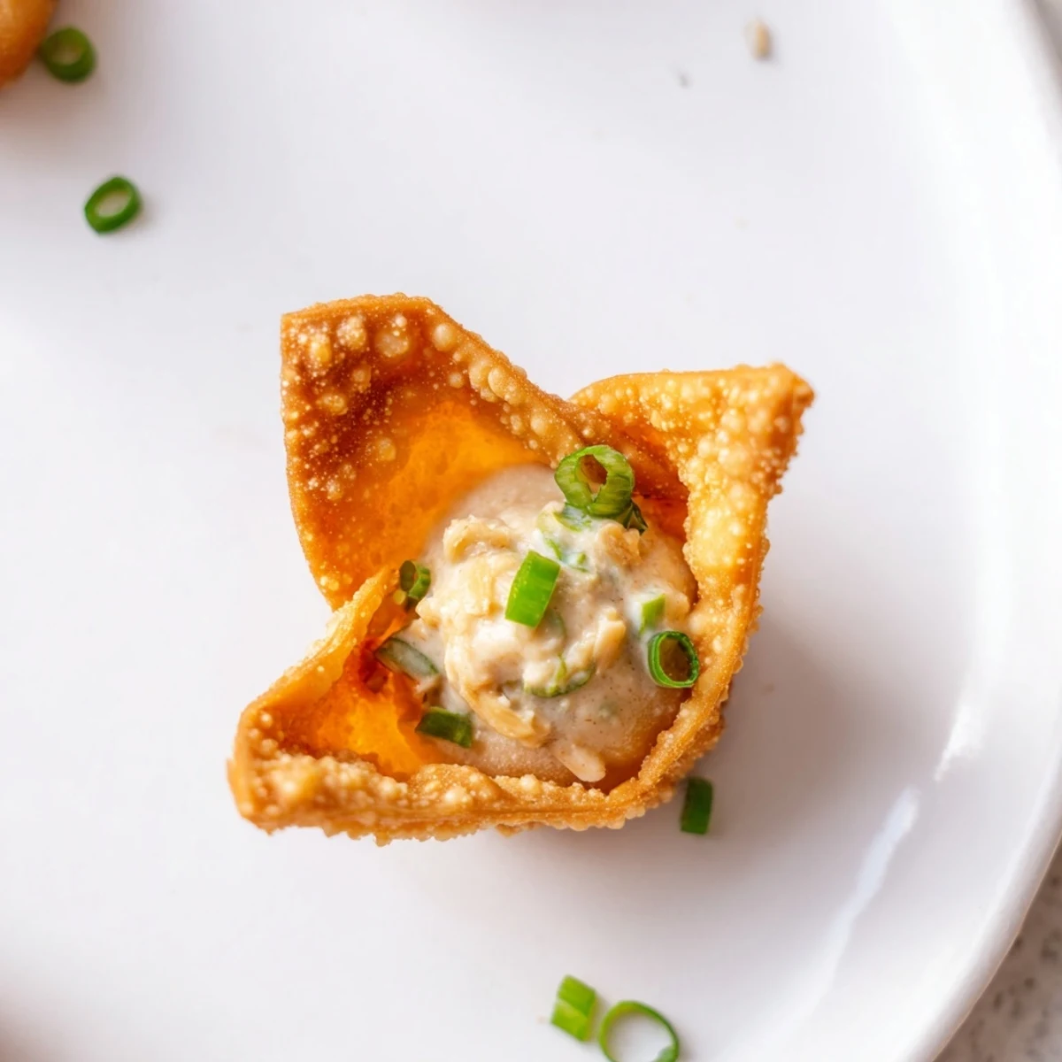 Golden-brown Crispy Crab Rangoon Bombs are arranged on a platter, their crunchy wonton wrappers revealing a rich, creamy filling dotted with crab and green onions.
