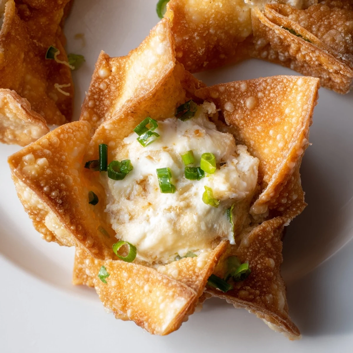 A serving plate of Crispy Crab Rangoon Bombs with a small bowl of sweet chili dipping sauce, garnished with fresh chopped chives.
