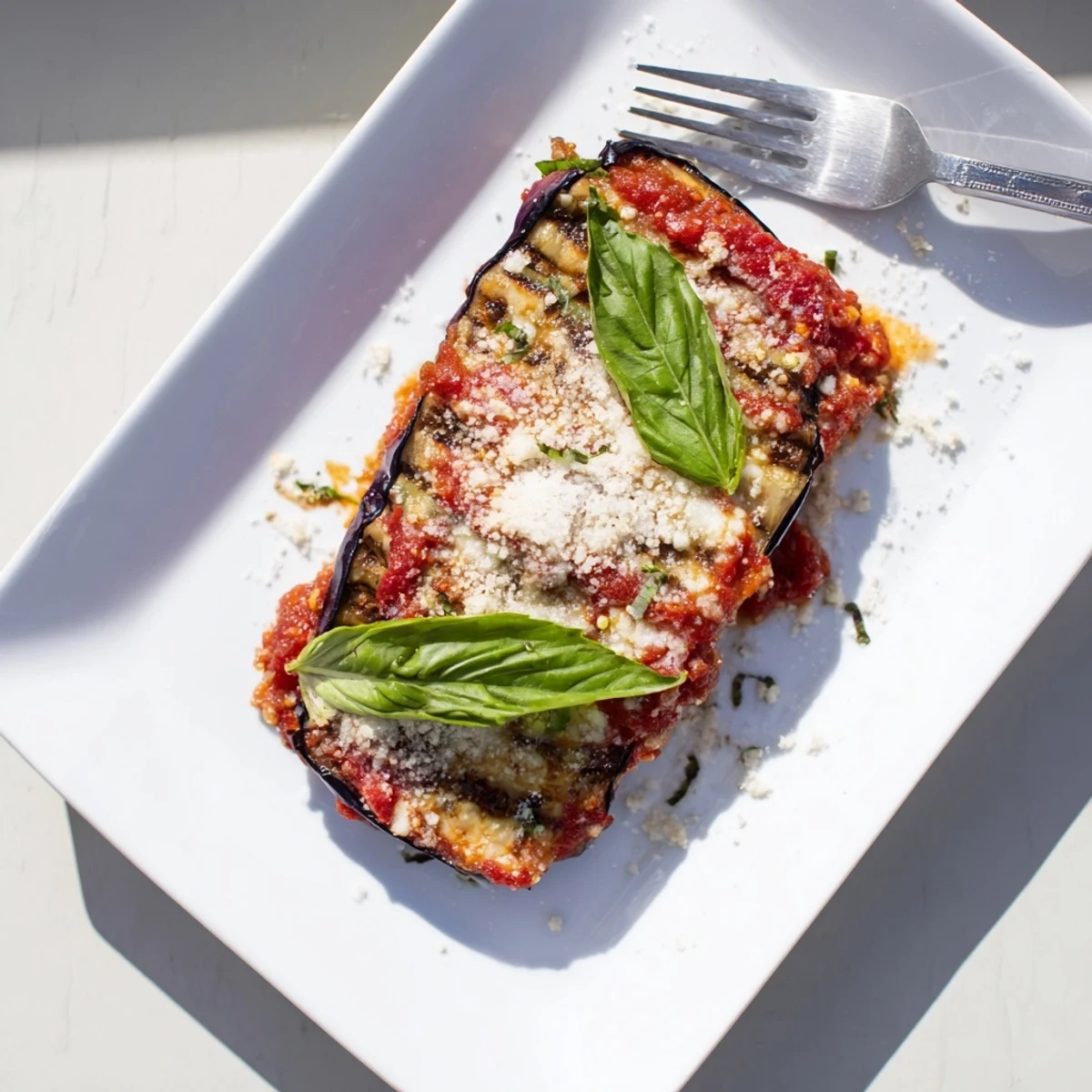 A close-up of Charred Aubergine Parmigiana, showcasing smoky grilled eggplant slices layered with bubbling mozzarella and rich tomato sauce.