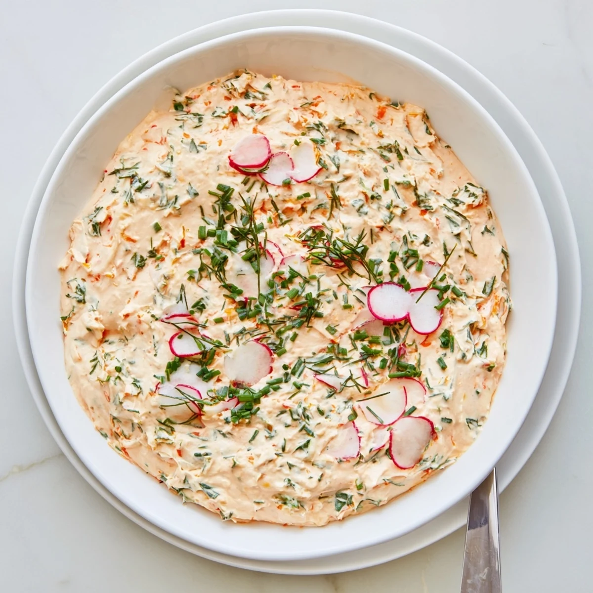 The Simple Easter Herb Cheese Dip sits in a rustic serving dish, with a cheese spreader nearby and a backdrop of Easter decorations for a festive gathering.