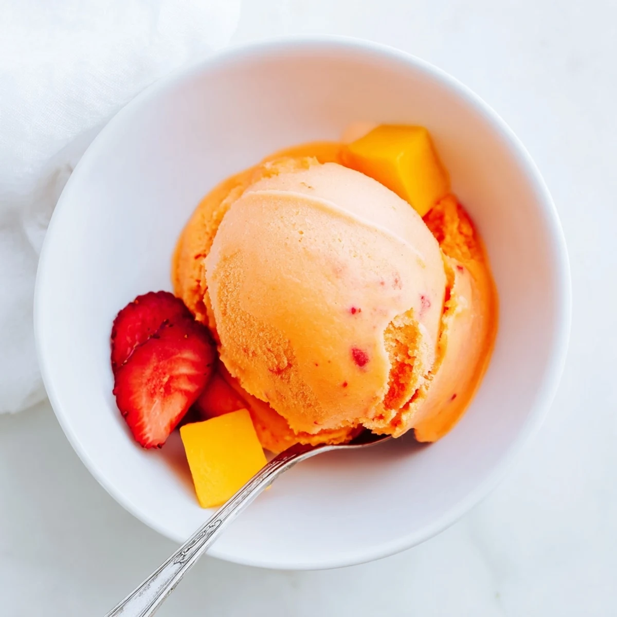 A spoon scooping Mango Strawberry Sorbet, revealing a smooth, icy texture and vibrant orange-pink hue.