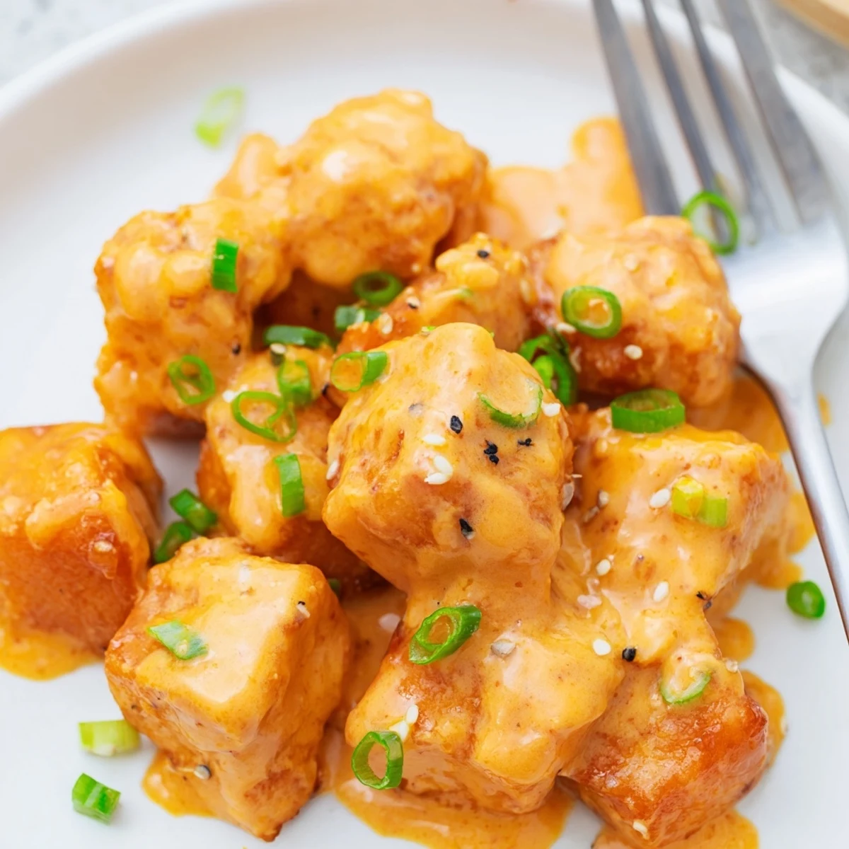 A serving plate of Bang Bang Salmon Bites garnished with sesame seeds, ready to enjoy as an appetizer.