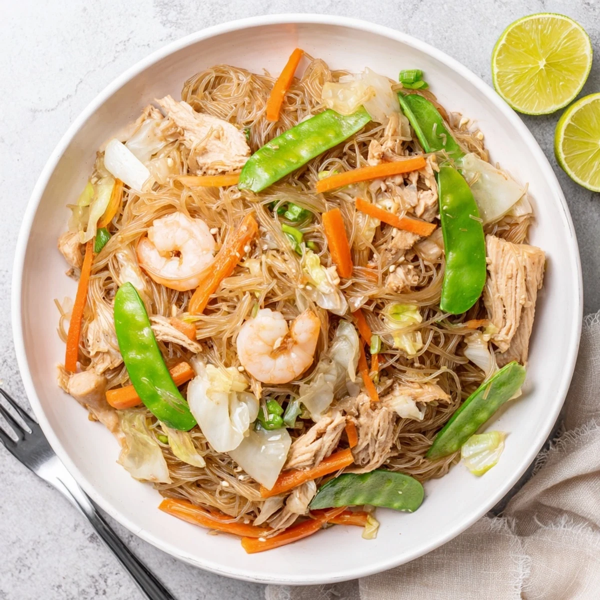 Golden pile of traditional pancit bihon garnished with fresh scallions and lemon wedges