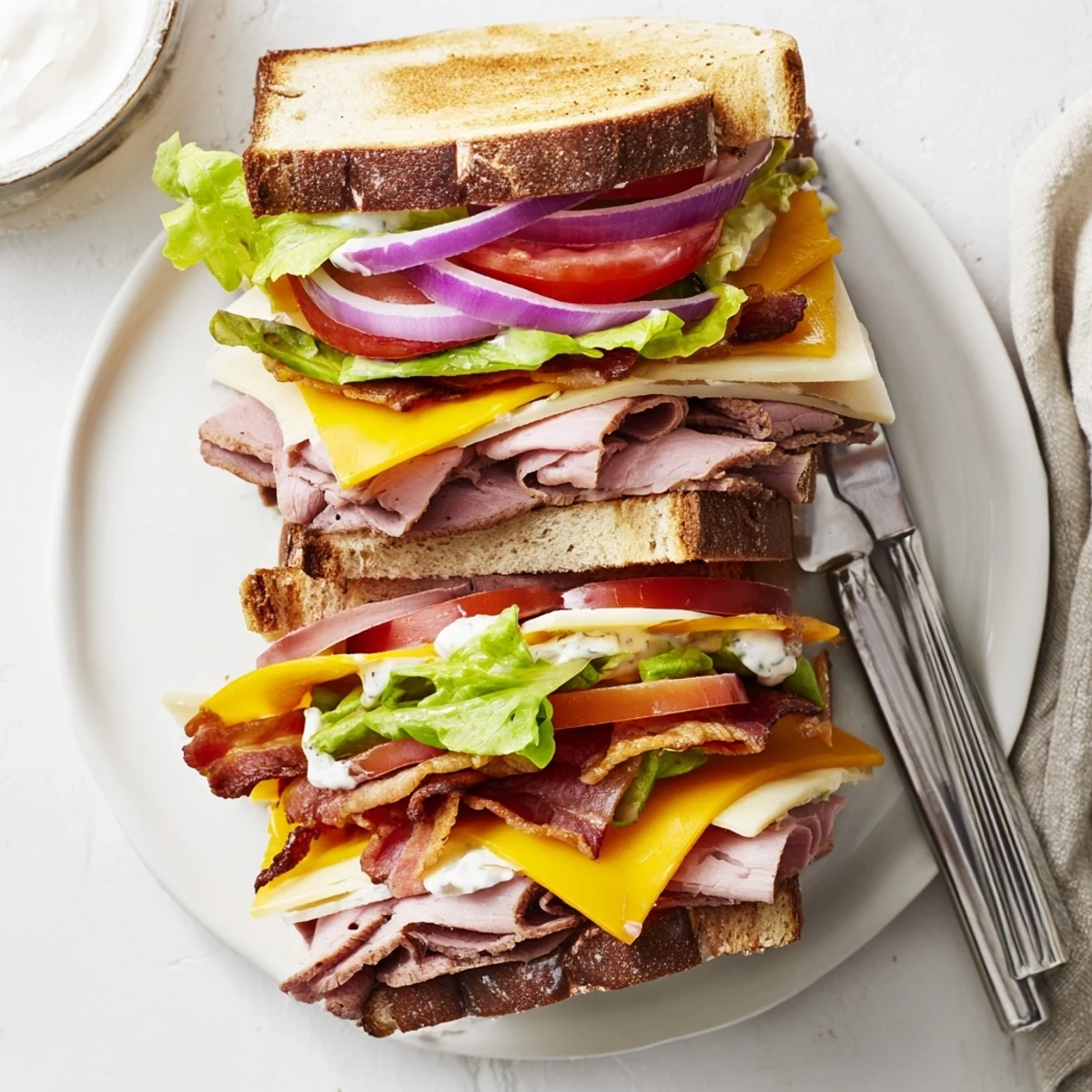 Hearty ultimate turkey beef bacon ranch sandwich on a plate with creamy ranch dripping from stacked deli meats and crisp vegetables