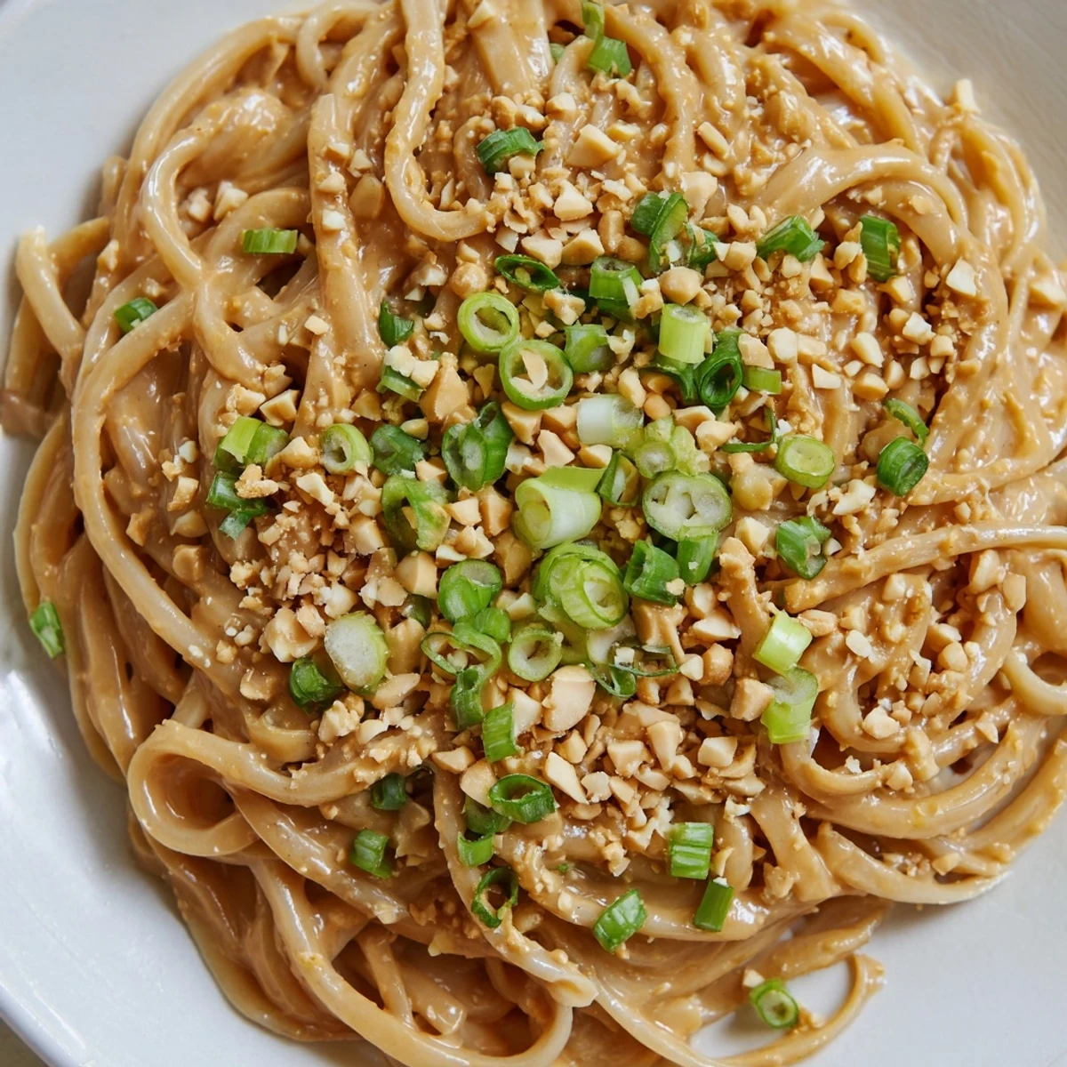 Close-up of savory sticky peanut butter noodles garnished with chopped cilantro and served in a white ceramic bowl.