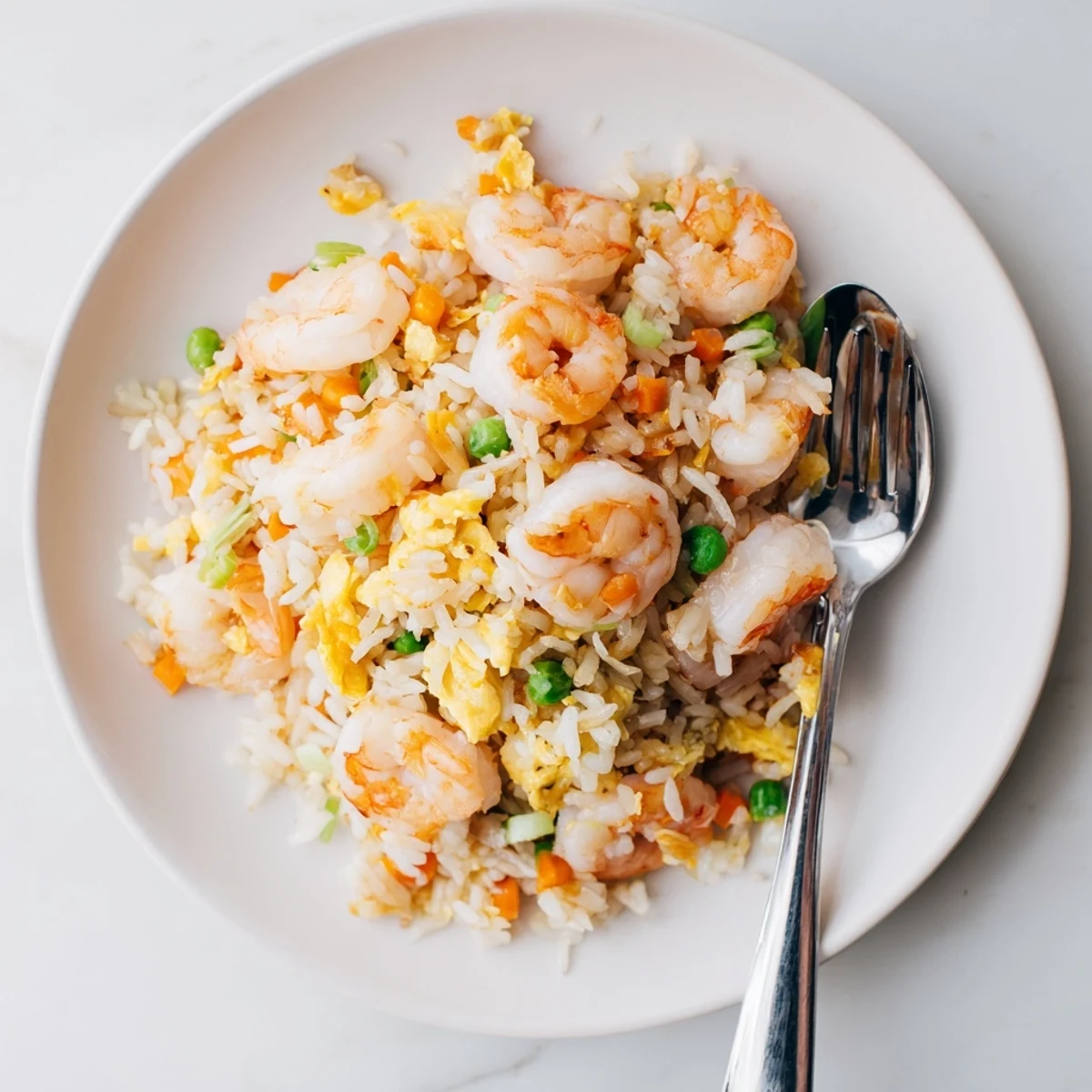 Golden shrimp fried rice with colorful peas, carrots, and fluffy scrambled eggs in a dark wok