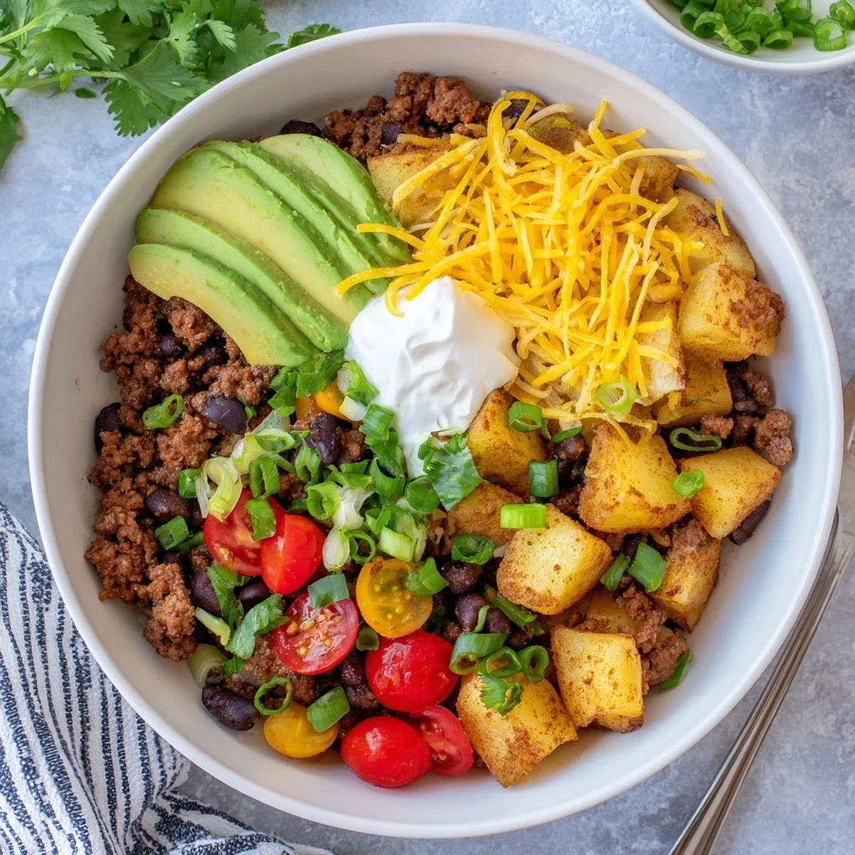 Hearty ground beef potato taco bowl layered with melted cheese avocado fresh tomatoes and crispy potatoes