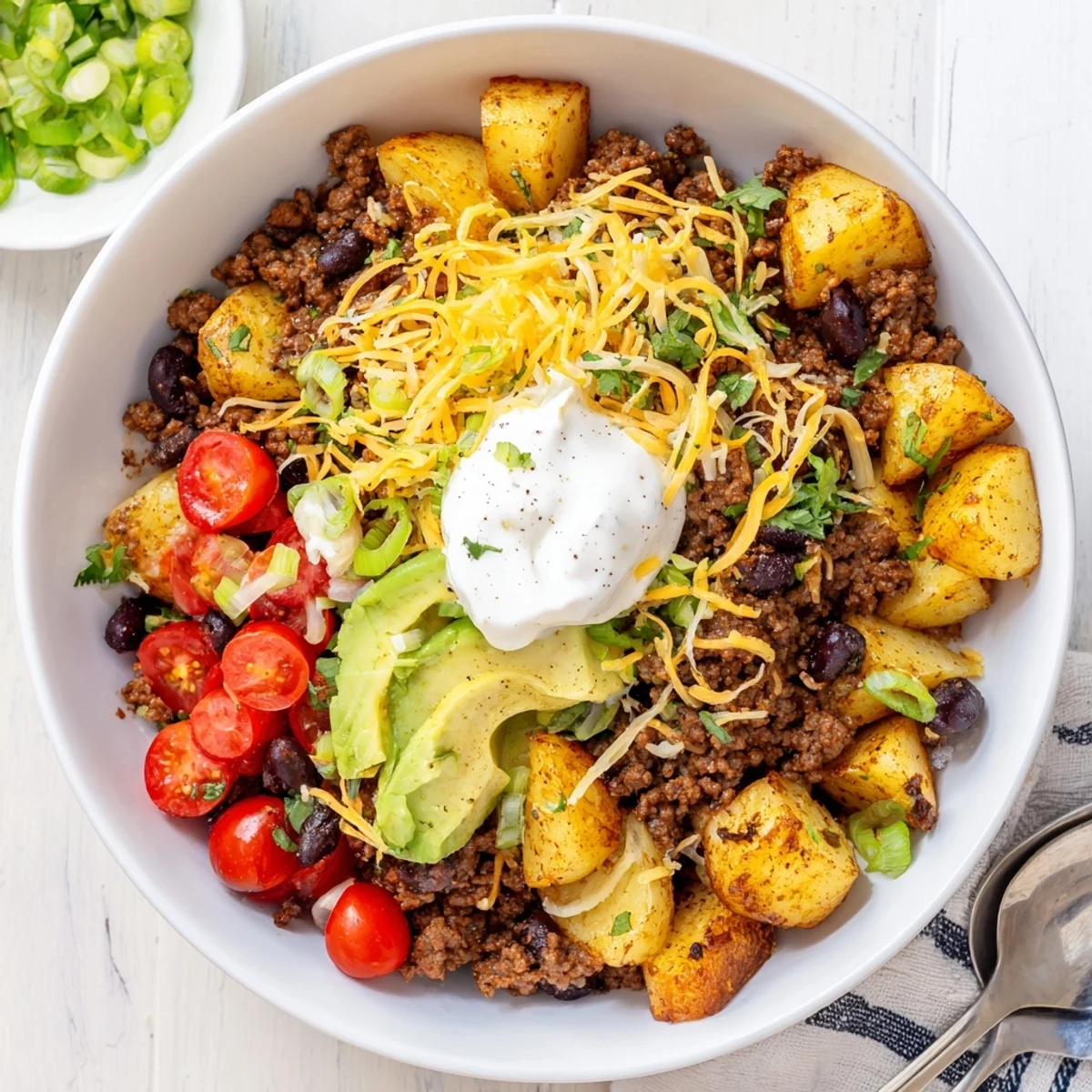 Tex-Mex style ground beef potato taco bowl served with sour cream cilantro lime wedges and black beans