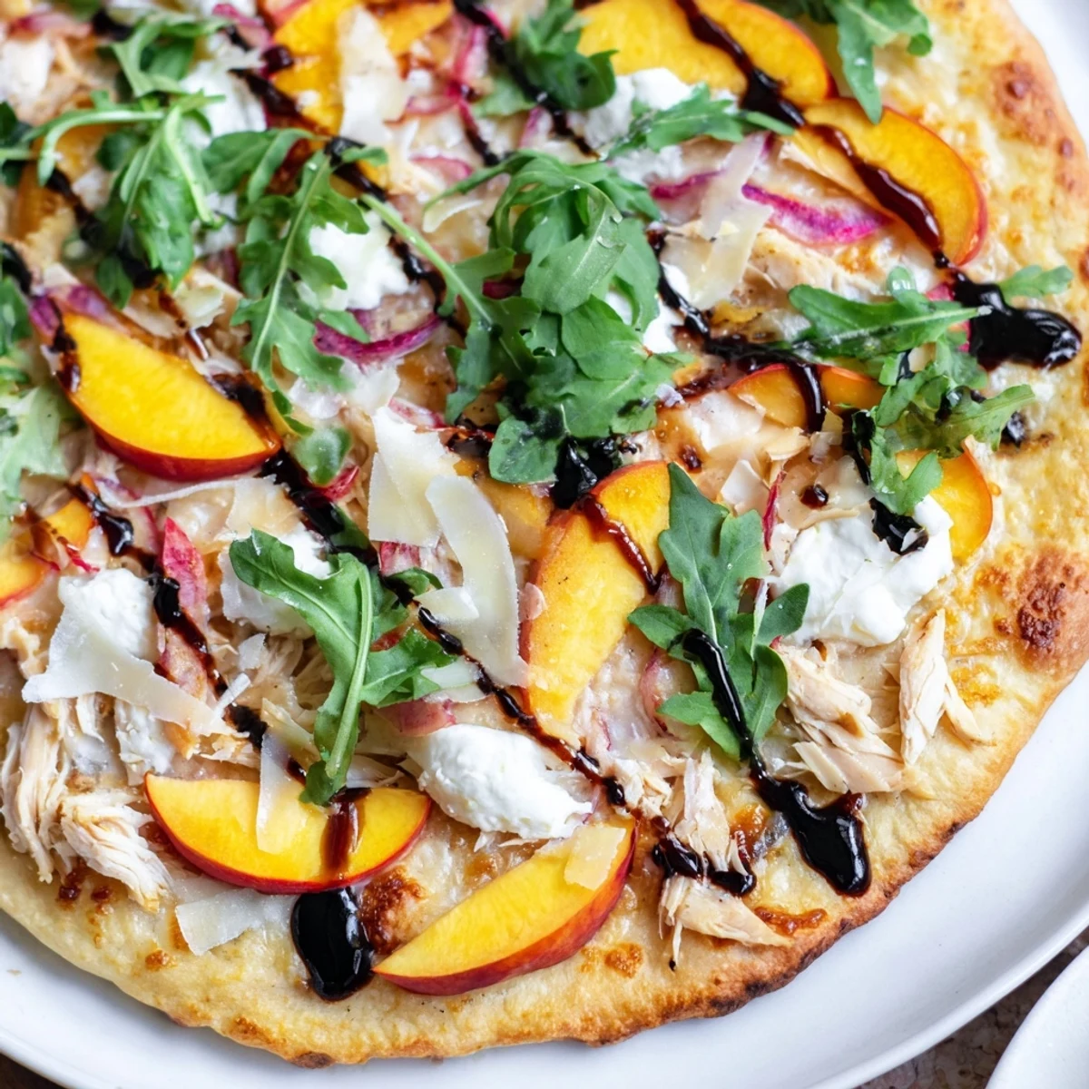 Golden Chicken Peach Ricotta Pizza topped with fresh arugula and drizzled balsamic glaze