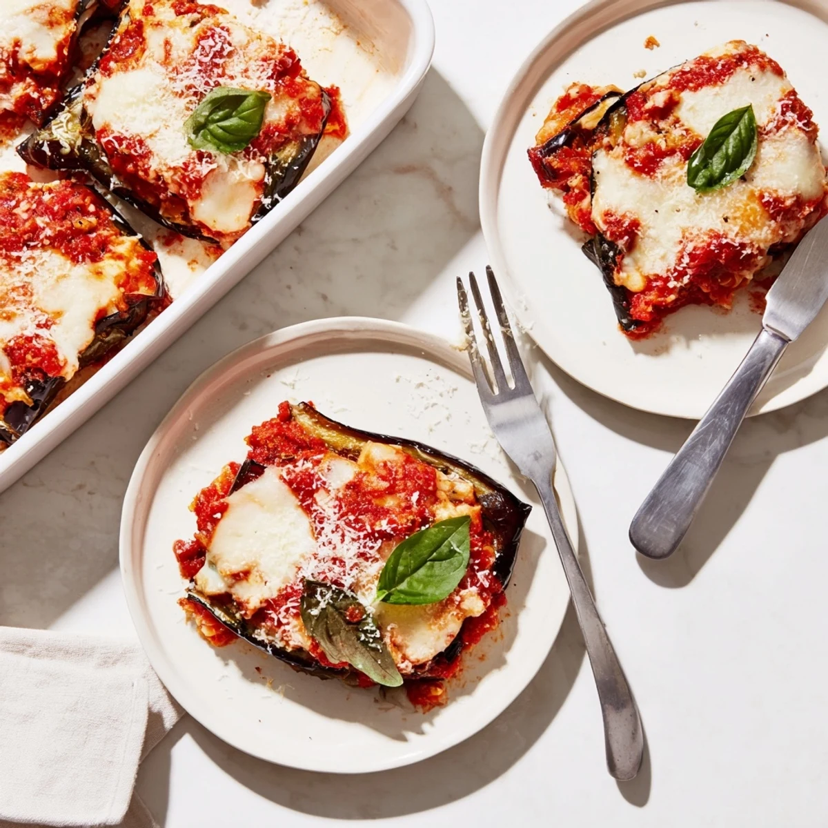Layers of roasted eggplant and creamy ricotta topped with tomato sauce in baking dish