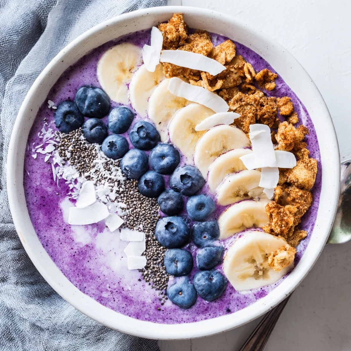 Creamy blueberry smoothie bowl topped with fresh berries, banana slices, crunchy granola and coconut flakes