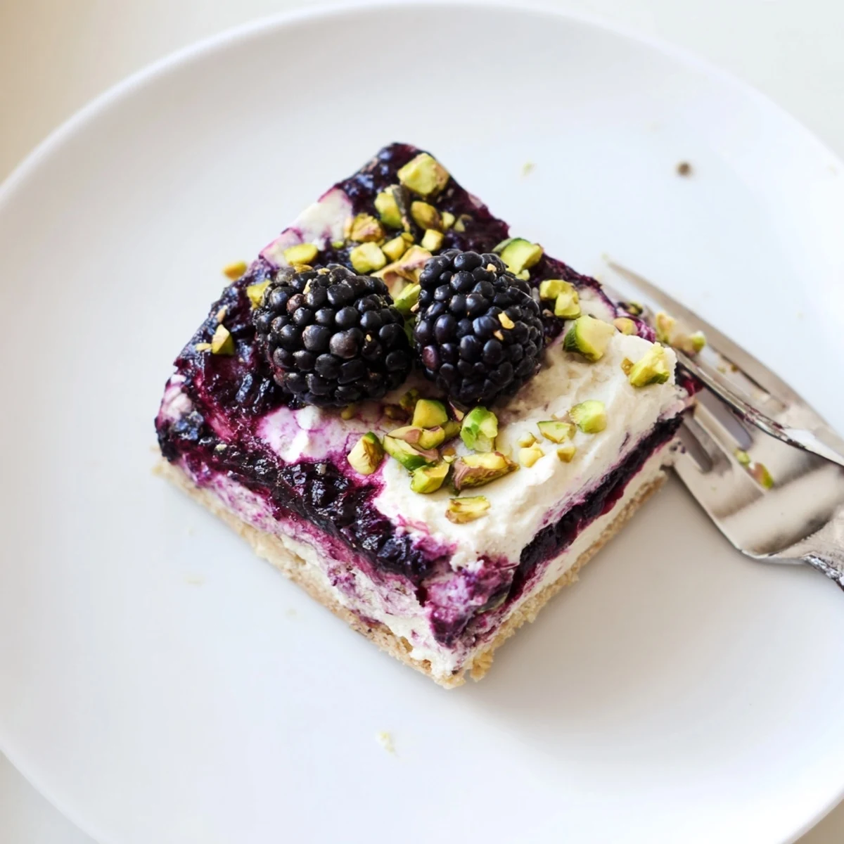 Golden square slice of Blackberry Pistachio Dream Bars topped with fresh berries and chopped pistachios