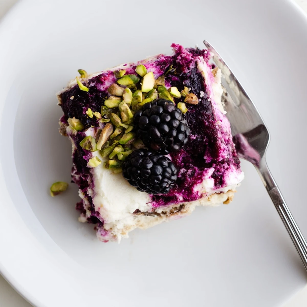 Layered dessert bar showing creamy cheesecake topping over vibrant blackberry compote on buttery pistachio shortbread crust