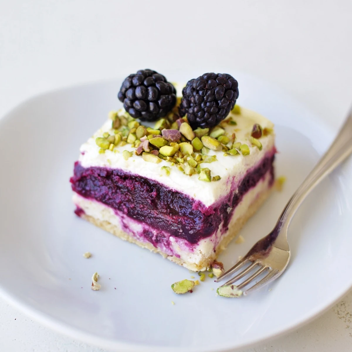 Chilled Blackberry Pistachio Dream Bars cut into squares with purple berry swirled through white cream filling