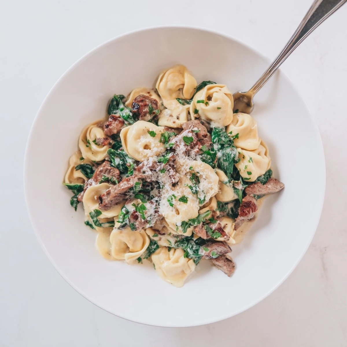 Creamy garlic steak tortellini dish featuring tender beef, pillowy cheese pasta, and wilted spinach in white sauce