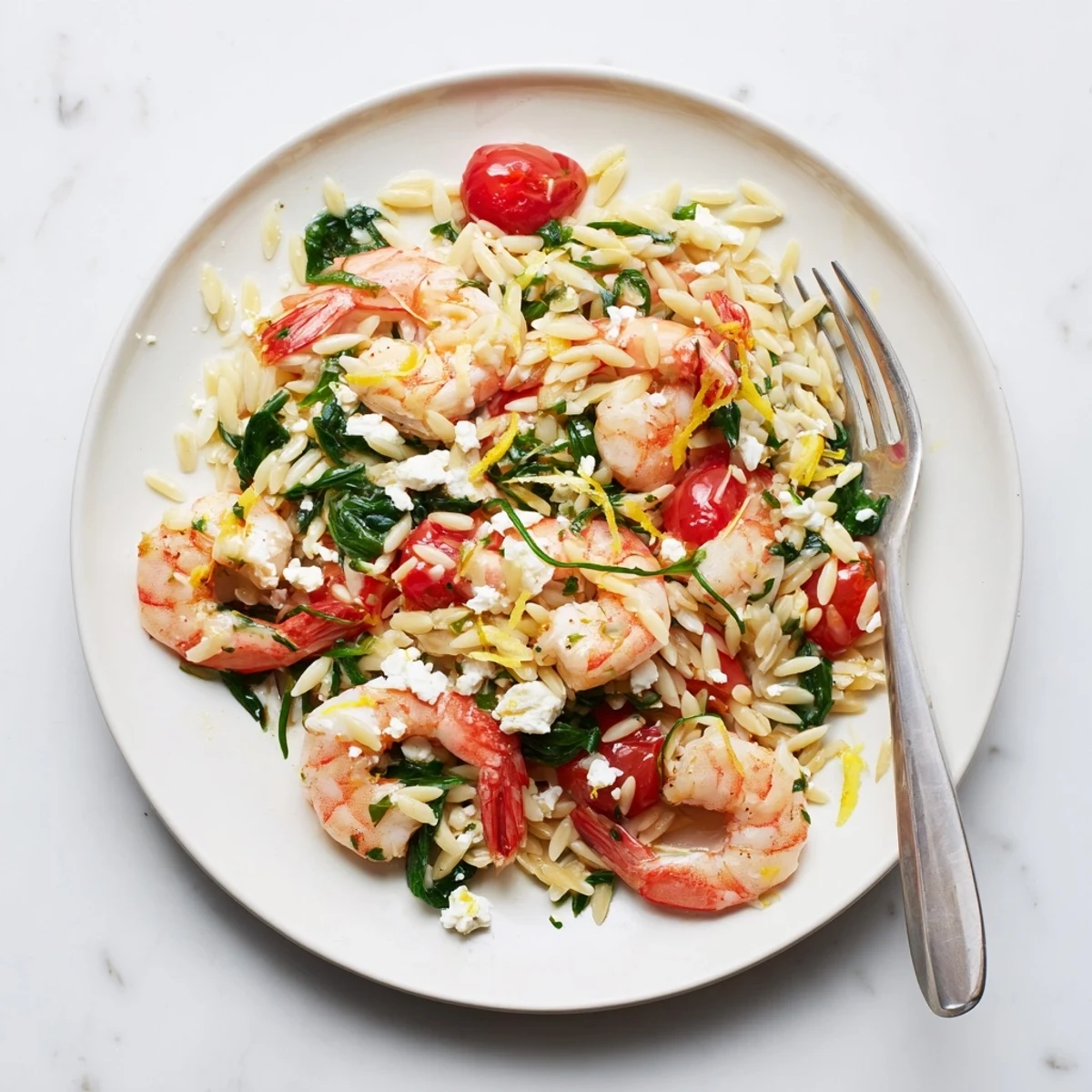 Golden lemon feta orzo shrimp plated with cherry tomatoes, spinach, and fresh parsley garnish