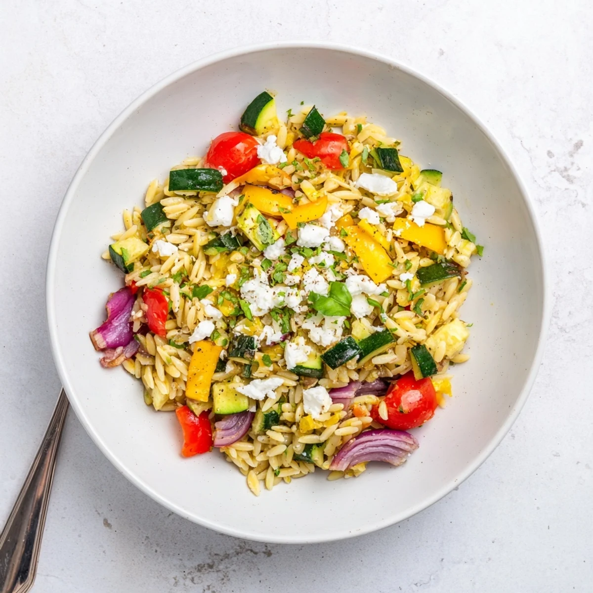 Hearty bowl of roasted vegetable orzo pasta topped with feta parsley and basil