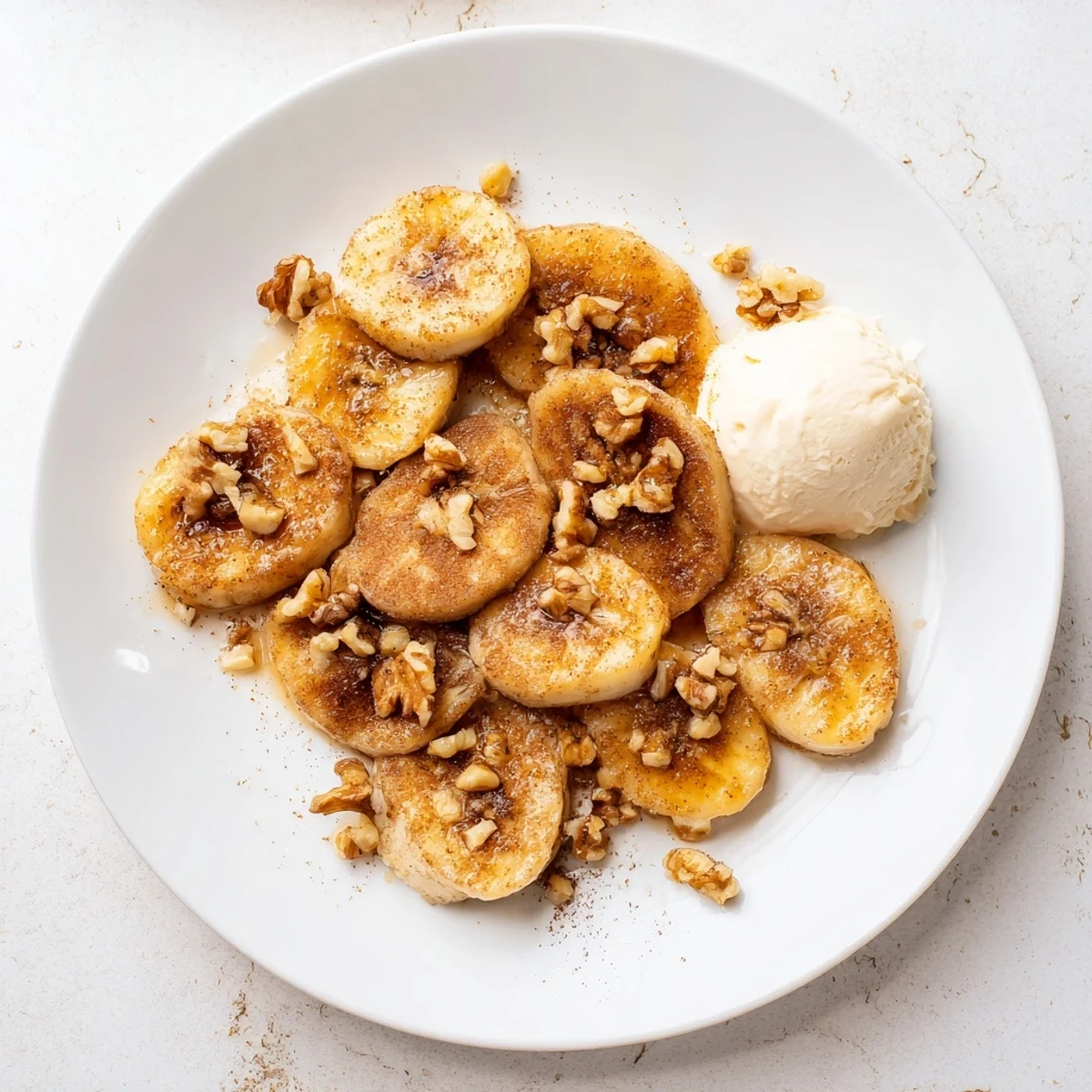 Warm pan fried cinnamon bananas arranged on a white plate topped with chopped walnuts and honey drizzle
