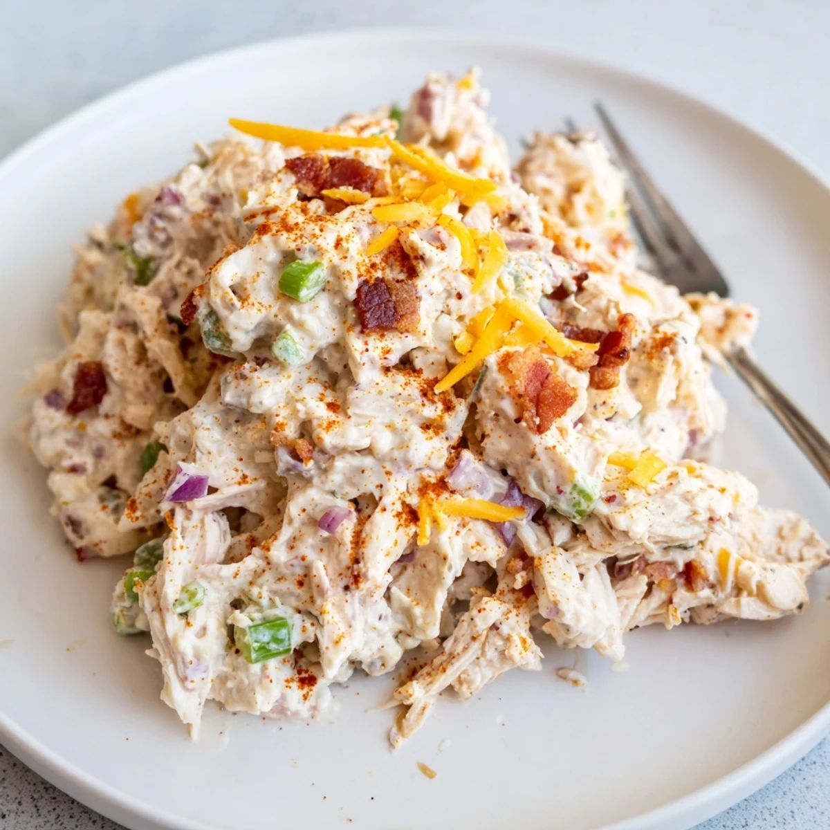 Spoonful of spicy low carb chicken salad with cheddar cheese crumbles and diced jalapenos on rustic wooden board