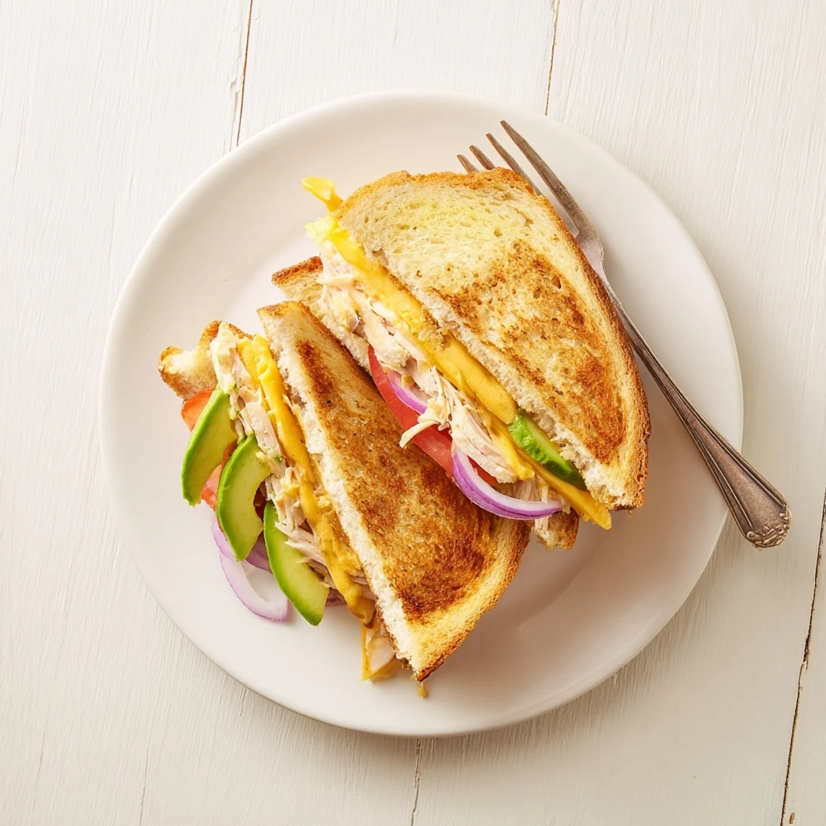 Savory chicken avocado melt sandwich cut diagonally displaying layers of creamy avocado ripe tomato and cheddar