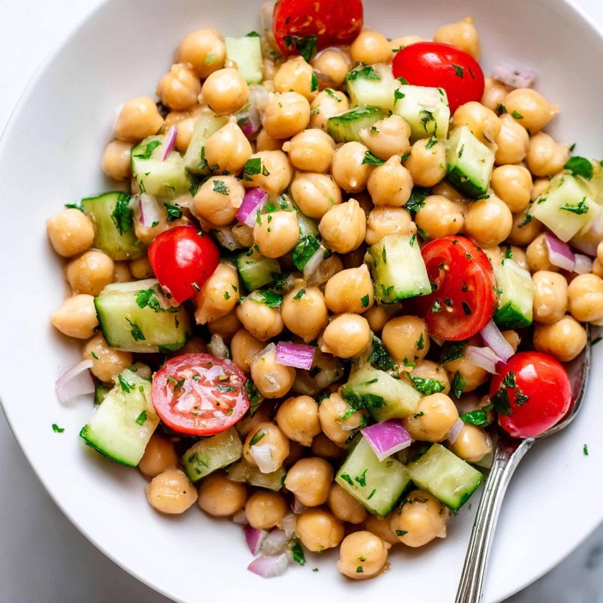 A close-up of chickpea cucumber salad served in a white bowl with fresh parsley