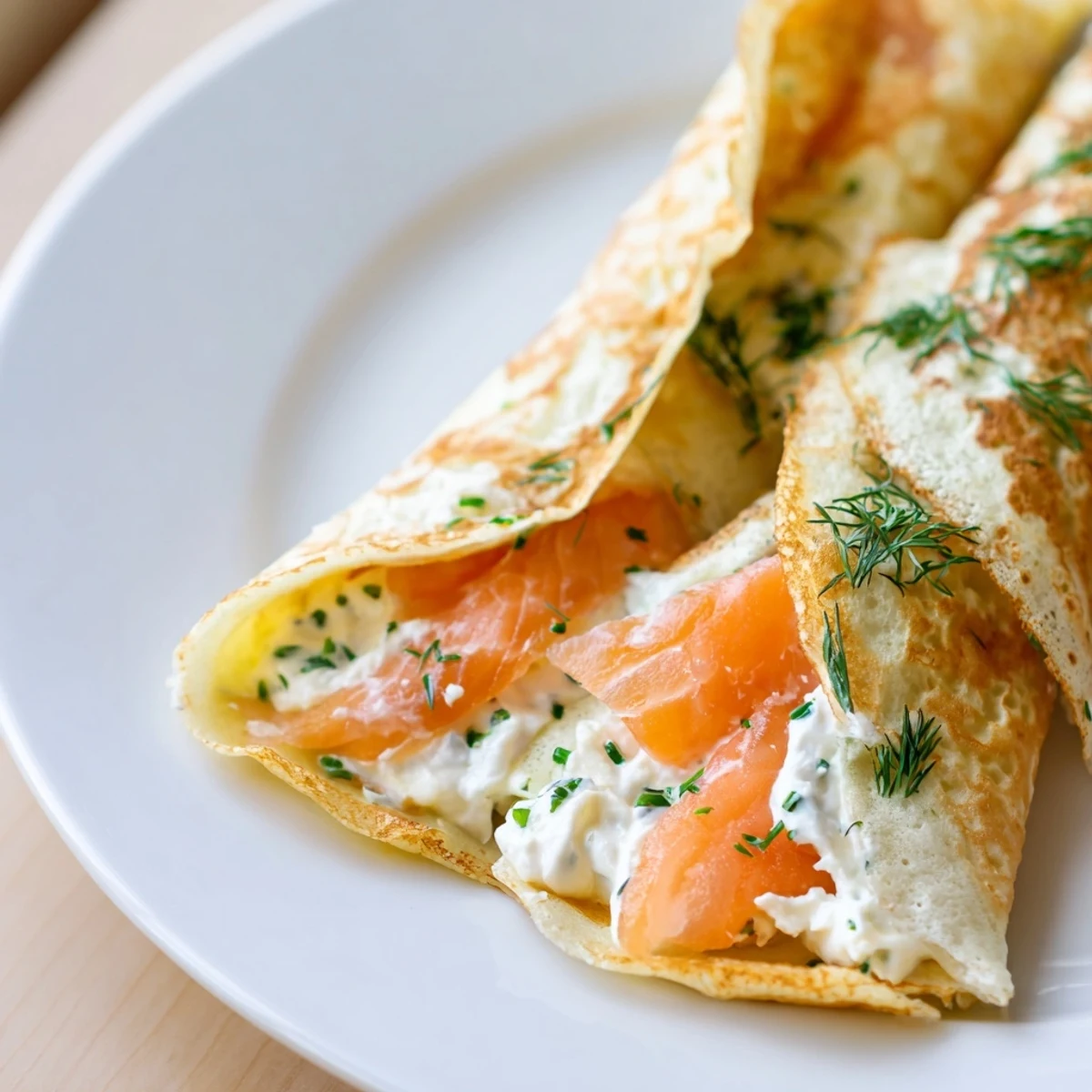 Golden smoked salmon crepes filled with creamy herbed cheese and fresh dill on a white serving plate