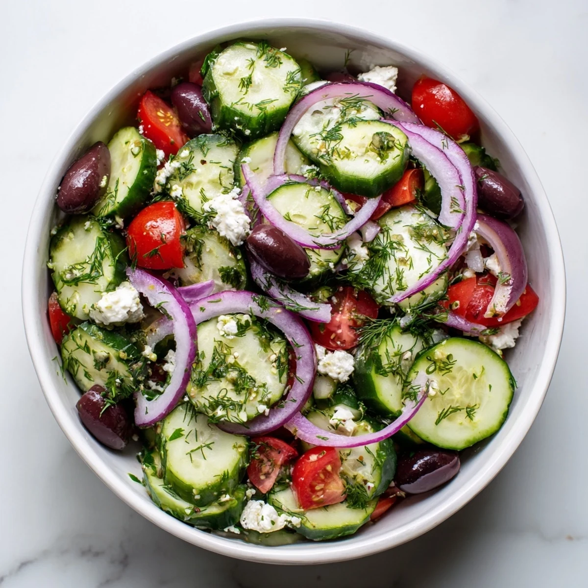 Fresh Mediterranean cucumber salad recipe with crisp vegetables, crumbled feta, and olives in a white bowl