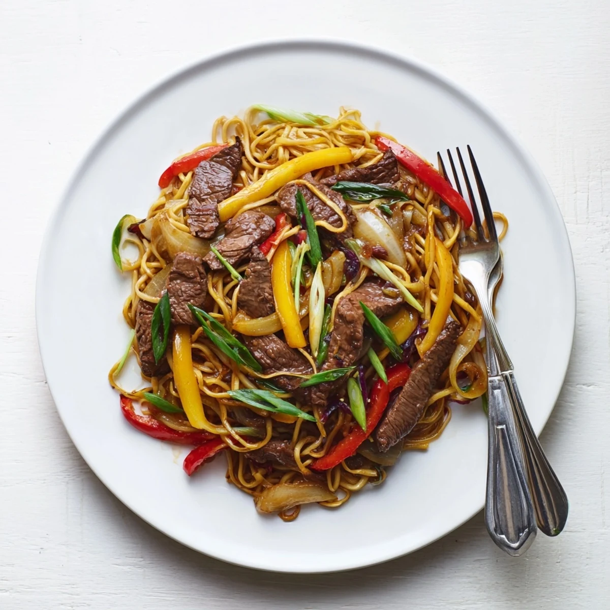 Steaming beef chow mein with colorful peppers and onions in a glossy savory sauce