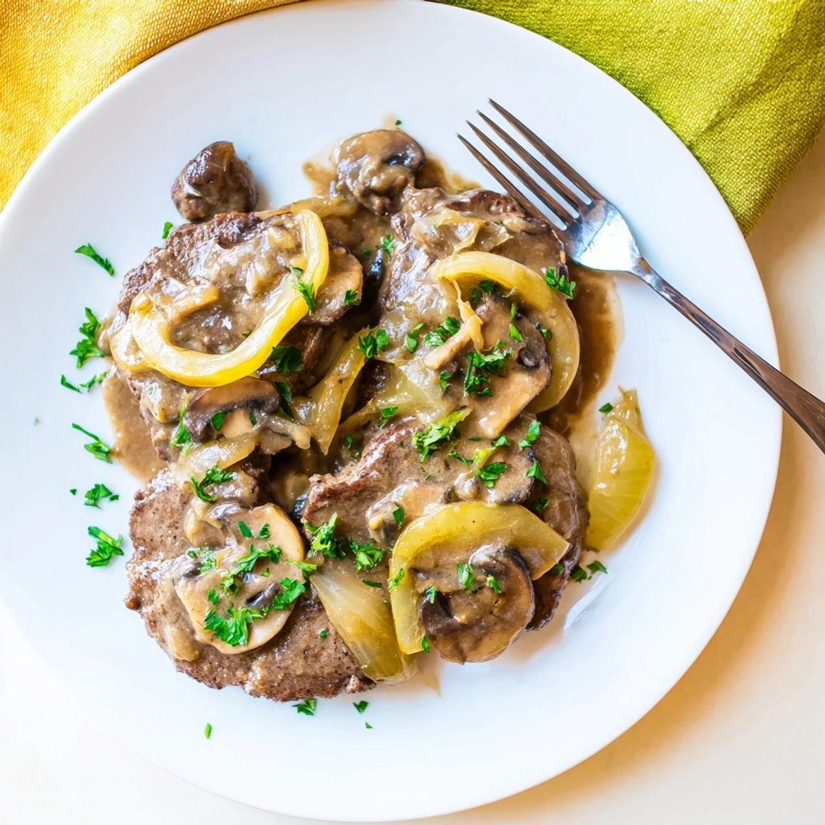 Fork-tender cube steak smothered in thick creamy mushroom gravy garnished with fresh chopped parsley