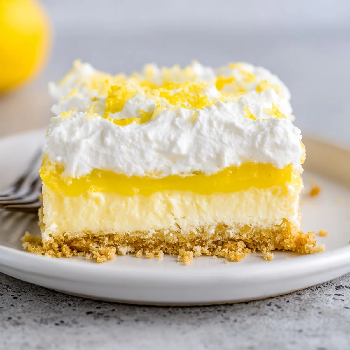 Slice of Lemon Lush Cake garnished with lemon zest, perfect with tea