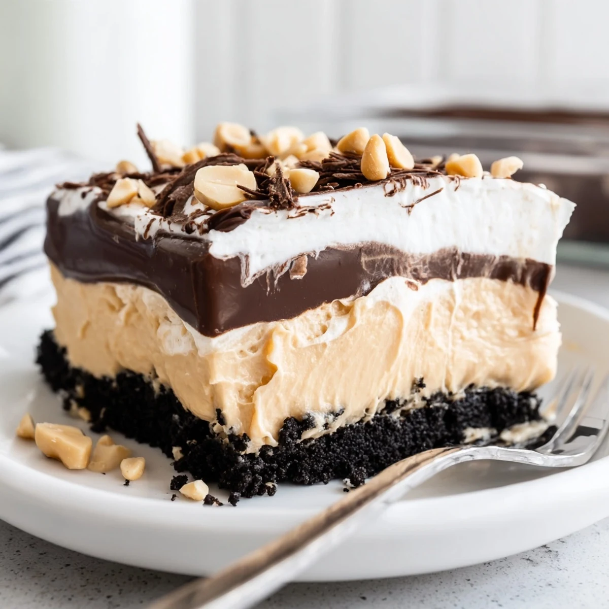 Peanut butter layered delight sliced into squares topped with whipped cream and peanuts