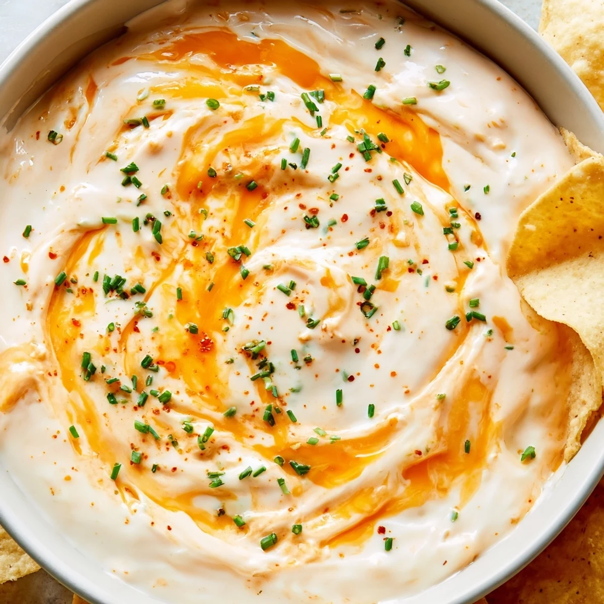 Warm cheese dip in a serving bowl garnished with fresh green chives