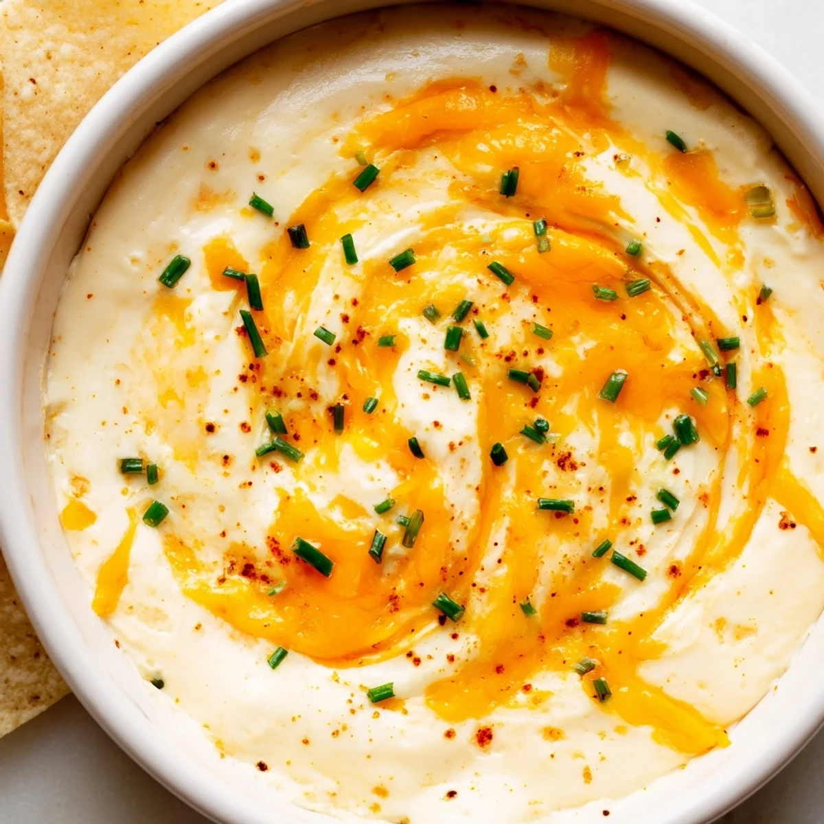 Creamy cheddar cheese dip poured into a bowl with tortilla chips alongside