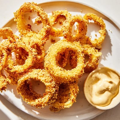 Golden, crunchy onion rings served with smoky chipotle mayo for dipping, a classic American snack.  