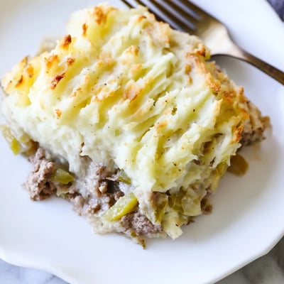 A close-up view of a slice of creamy mushroom and leek shepherds pie on a white plate, revealing the savory vegetarian filling.