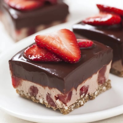 Smooth chocolate shell glazes chilled cheesecake bars topped with vibrant halved strawberries for a decadent treat.