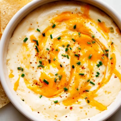 Creamy cheddar cheese dip poured into a bowl with tortilla chips alongside